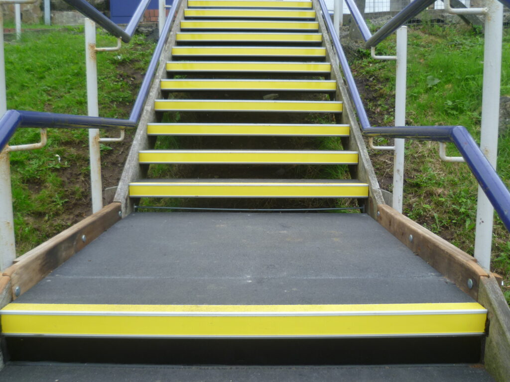 black stair tread cover with yellow nosing on a set of steps in a car park