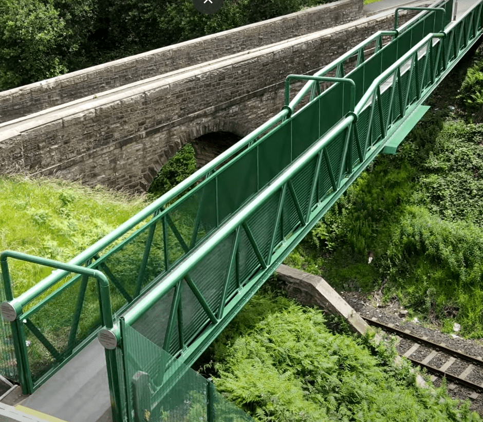 a pedestrian footbridge over a railway line with powder coated green mesh infill panels either side of the footbridge for safety reasons