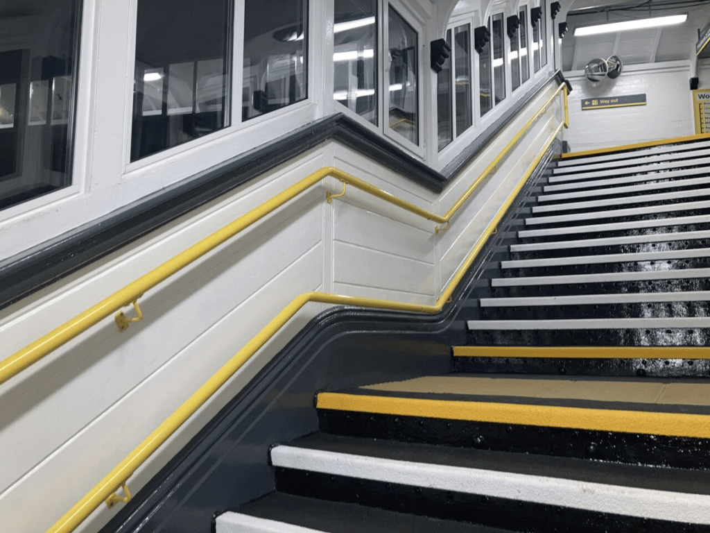 white and yellow anti slip nosing on a set of stairs, with a yellow handrail